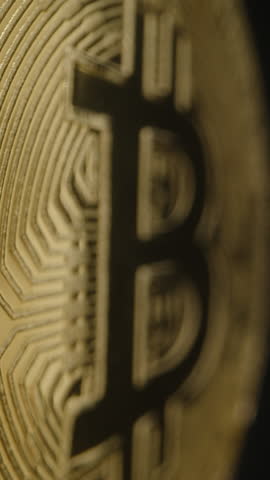 Vertical video. Bitcoin Coin Rotating Slowly as Its Golden Surface Reflects Bright Light. The Bold "B" Logo and Detailed Circuit Patterns Shine Brilliantly Against a Black Background.