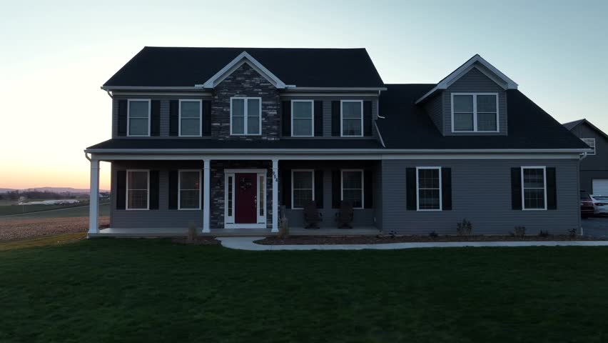Large Farmers House with porch on property in rural countryside of USA. Sunset time at horizon with sun reflecting on house wall. Aerial revealing shot.