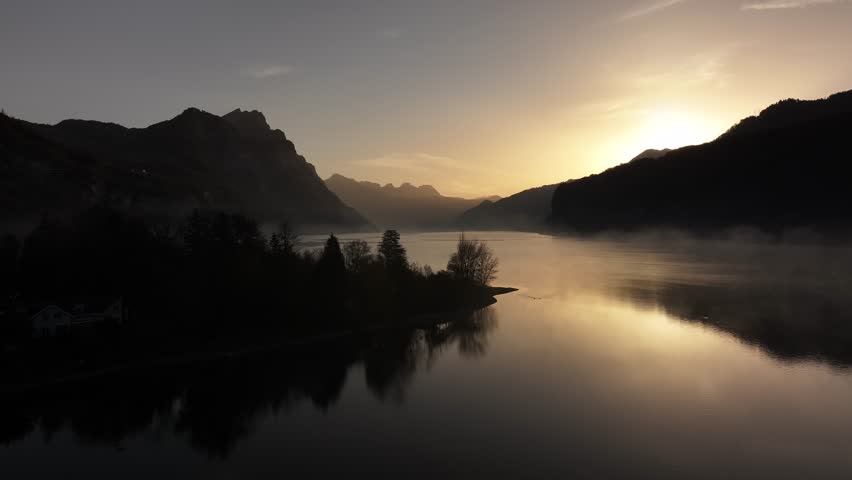 Serene morning at Walensee, Switzerland, with mist over lake and sun rays illuminating mountains as camera slowly pushes in, tranquil beauty of Swiss landscape.