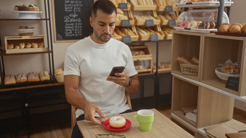 Young hispanic man in cafe taking photo of breakfast with smartphone in a bakery