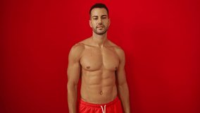 Young hispanic man shirtless in swimsuit, pointing cheerfully with a natural smile and upward finger gesture over isolated red background - Powered by Shutterstock - Get 15% off with code: PIKWIZARD15