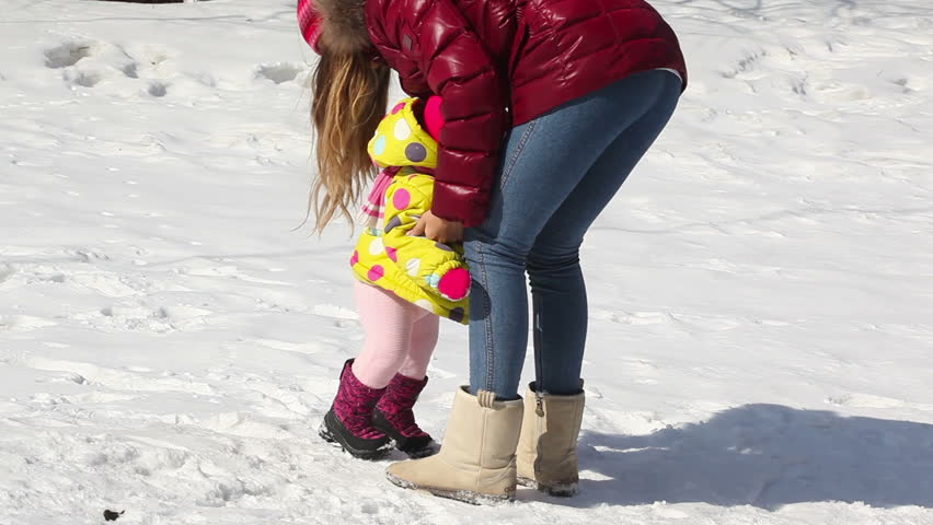 Small girl falls down on snow and mother cares of her