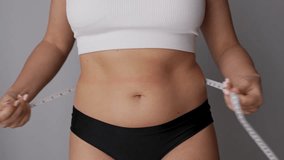 A young woman measuring her belly with a measure tape on a grey background. Diet concept. Overweight, excess weight, weight gain, eating disorder. Belly girth - Powered by Shutterstock - Get 15% off with code: PIKWIZARD15