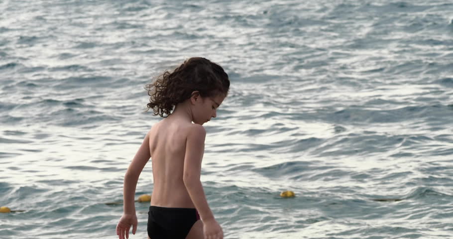 A little boy in a swimsuit joyfully throws stones into the sea, creating playful splashes.
