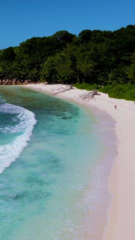 Visitors stroll along the vibrant shoreline of La Digue Seychelles, enjoying the warm sun and soft sand. The turquoise waters gently lap against the pristine beach, creating a serene atmosphere.