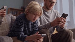 Low angle view of mother, father and teenage boy checking their smartphones while resting on cozy sofa at home - Powered by Shutterstock - Get 15% off with code: PIKWIZARD15