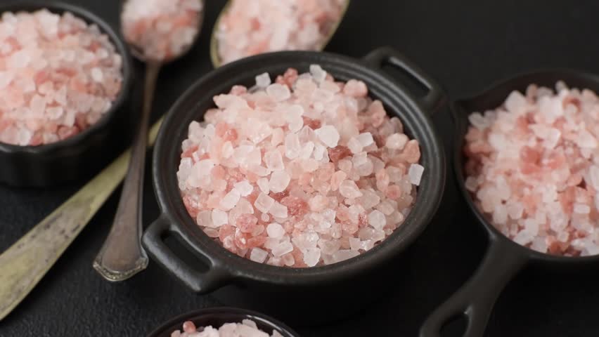 Pink himalayan salt in a black bowl on a dark concrete background. Seasonings and additives in the kitchen