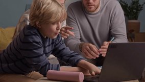 Handheld shot of caring Caucasian parents helping their teenage son with homework while sitting all together in front of laptop screen at home - Powered by Shutterstock - Get 15% off with code: PIKWIZARD15