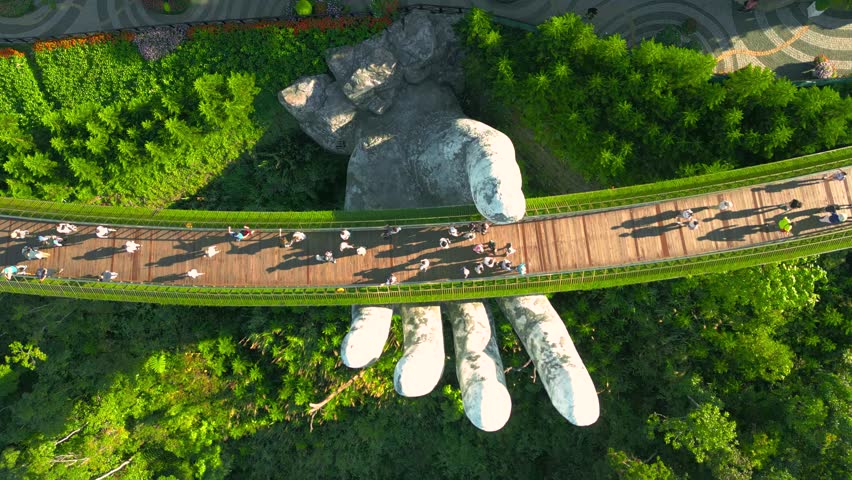 The stunning Golden Bridge at Ba Na Hills, Vietnam, is held aloft by the intricately designed "Hands of God", surrounded by lush greenery. Aerial drone view.
