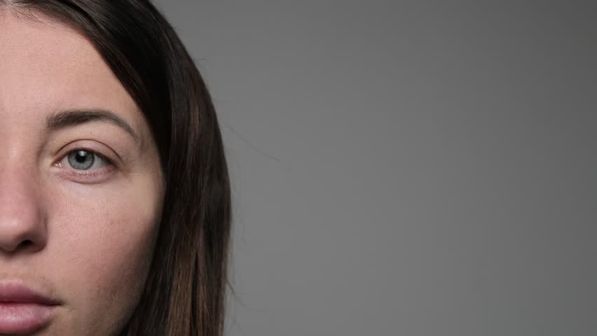 Close-up of a woman with long dark hair squinting her eyes, showing facial lines and natural skin texture, expressing discomfort or concentration.
