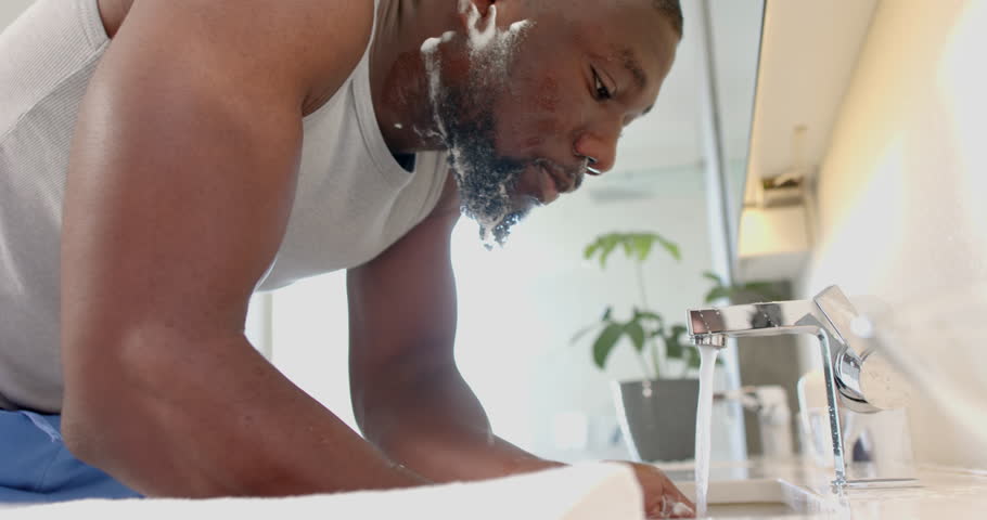 Washing face in bathroom, strong and fit African American man enjoying self-care. hygiene, grooming, skincare, healthy lifestyle, well-being, daily routine, unaltered, slow motion