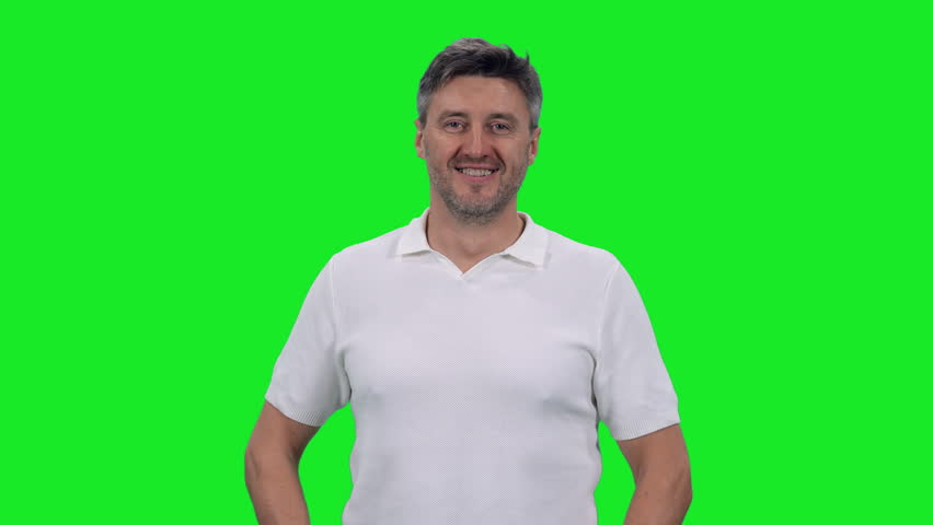 Smiling middle aged man in white t-shirt standing with arms crossed on chest against green chroma key background, 4k pre-keyed footage