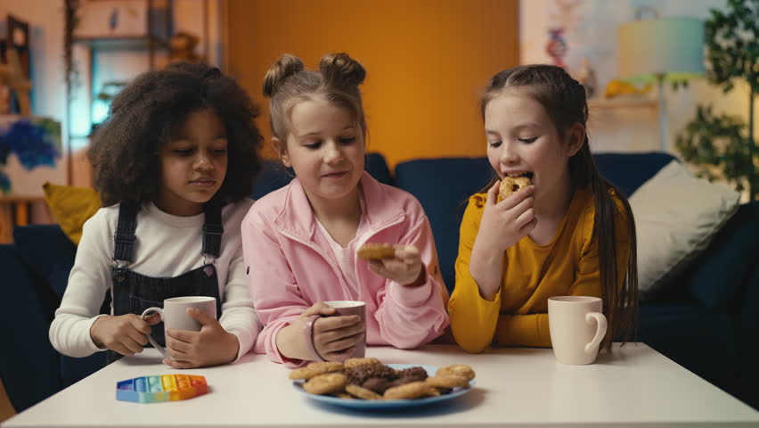 Happy little girls eat cookies and drink tea together, enjoying a friendly lunch