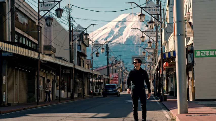 A captivating scene of a man walking along Honcho Street in Shizuoka city, Japan, with the majestic snow-covered Mount Fuji in the background.