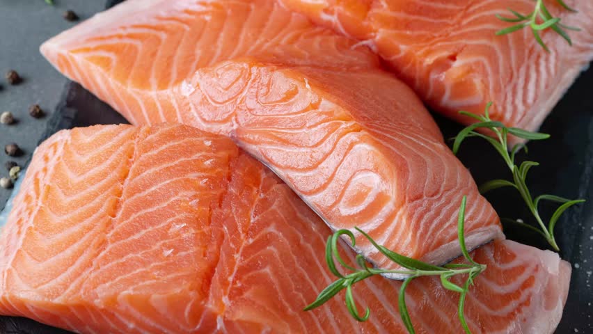 Raw salmon fillet and ingredients for cooking, seasonings and herbs on a dark background.