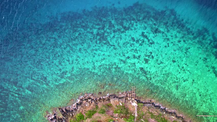Aerial top down pan along vibrant tropical vegetation to serene turquoise waters sloping into the abyss, St. Thomas, USVI