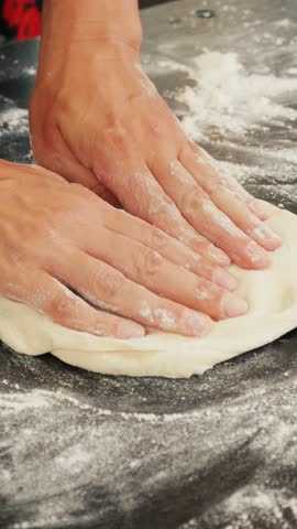 Hands preparing dough for pizza on table. Woman kneading dough for pizza base in modern kitchen. Cooking traditional italian pizza. Making homemade bread. Vertical video