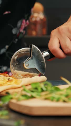 Cutting pizza with round cutter knife, close up. Delicious cheese pizza being cut into pieces. Female slicing pizza with cutter. Vertical video