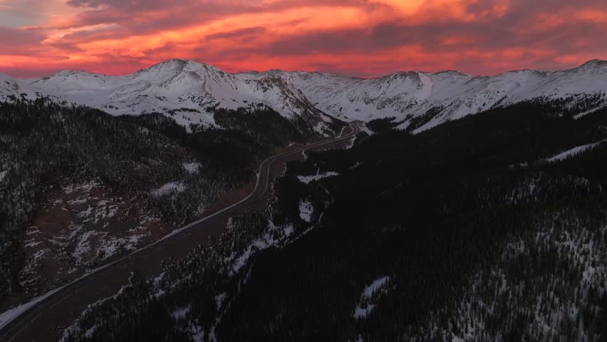 Rocky Mountains aerial drone i70 highway Winter solstice Colorado vibrant orange red cloudy skies setting sunset cars trucks traffic Coon Hill Parshall Eisenhower tunnel Continental Divide pan forward