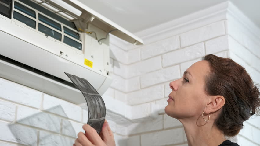 Woman clean the split system. A view of happy female try to clean the split system from the modern new air conditioner at home.