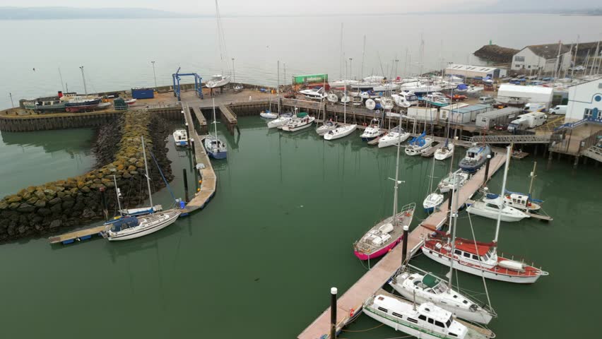 Reversing overhead aerial shot of Carrickfergus Marina in Northern Ireland. The camera shows boats resting in the green water. Produced in 4K, 60FPS and in Rec709 colour.