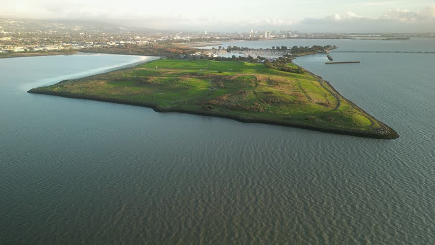 Aerial view of Cesar Chavez Park, a peninsula extending into the San Francisco Bay, featuring grassy fields, a shoreline, and the cityscape of Berkeley in the distance