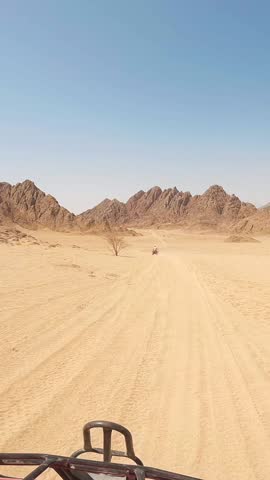 Vertical tourist in keffiyeh driving fast atv bike in the wild Egypt desert on excursion. Sand mountains in the horizon and clear blue sky.