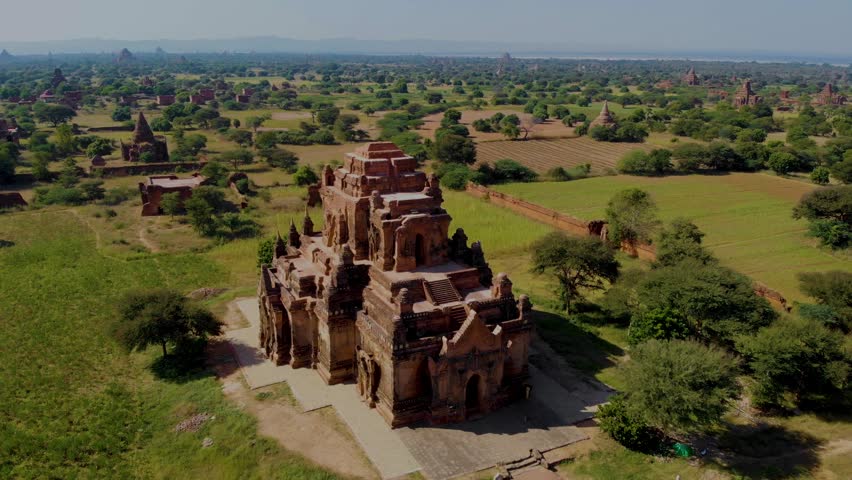 Discover the awe-inspiring temples and pagodas of Bagan Myanmar as sunlight bathes the landscape in warmth. Green fields stretch endlessly, adorned with ancient architecture.