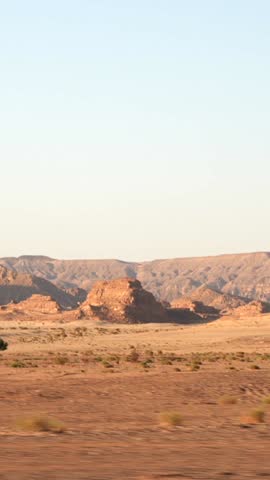 Vertical side view from the window of moving car to the bedouin village in the desert between sandy mountains. African road trip through the Sahara