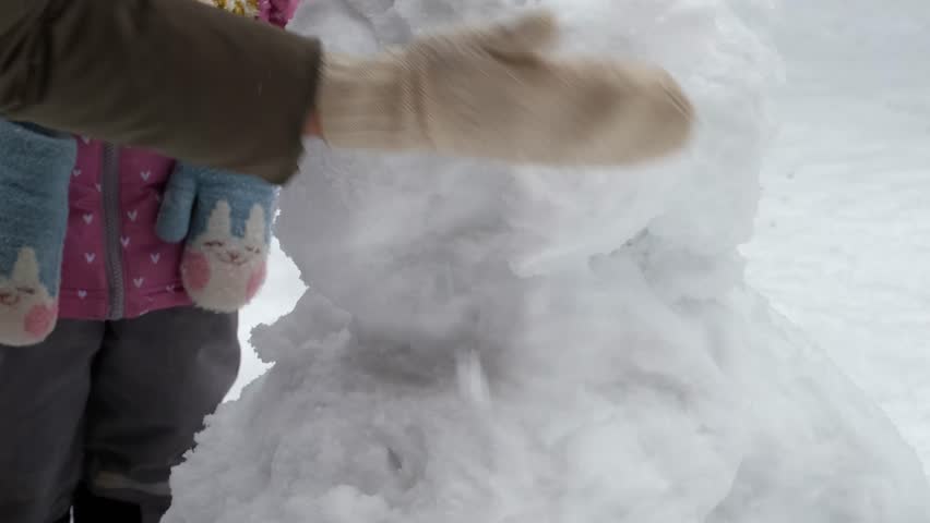 A loving mother and her young daughter build a snowman together in a winter wonderland. Their mitten-clad hands carefully shape snowballs, creating joyful memories in the frosty outdoors.