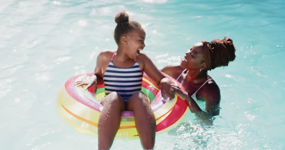 Playing in pool, mother and daughter enjoying summer day with inflatable ring. african american family, swimming, fun, leisure, outdoors