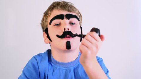 Little boy imitates pipe smoking and he has fake mustache, eyebrows, beard and sideburns