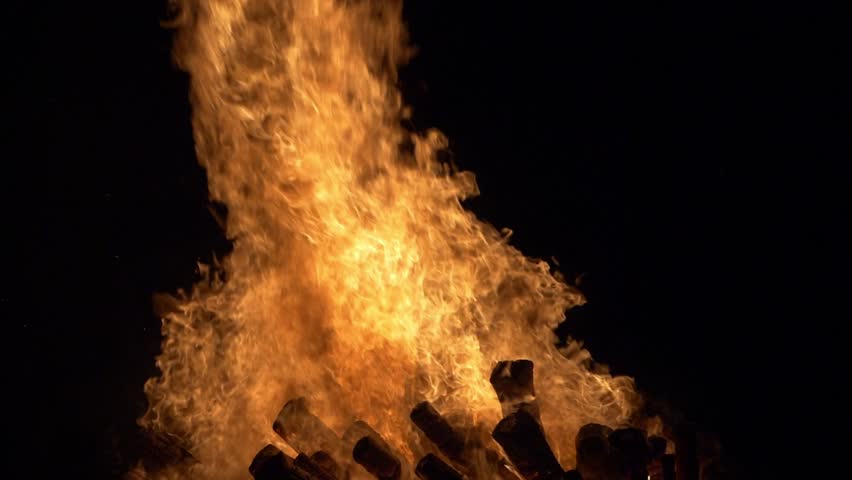 Large, crackling flames consume wood in a striking nighttime fire scene. Slow