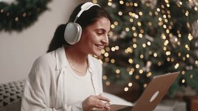 Charming indian woman relaxing at home listening music or working online browsing products in internet store on laptop computer on bed near Christmas tree at holidays indoors - Powered by Shutterstock - Get 15% off with code: PIKWIZARD15