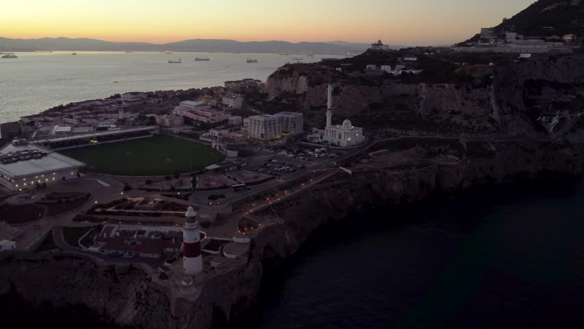 Aerial view of Gibraltar at sunset. Street lights on. Europa Sports Complex Stadium with night light on. Travel destination. Bay of Gibraltar. City of Gibraltar and La Linea, in background. Track left