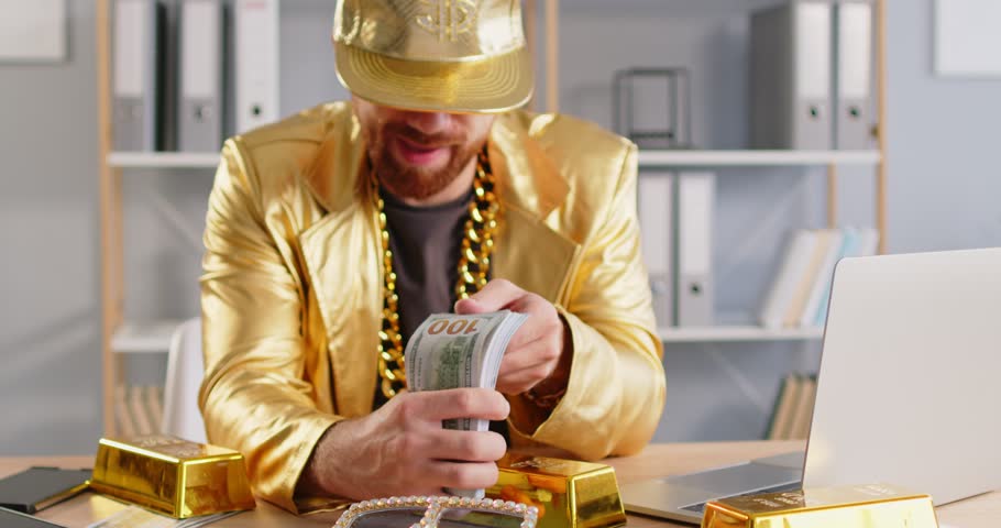 Funny extravagant rich happy man holding wad of cash, shining golden jacket, massive chain around neck. Producer showing impressive achievements lottery winner, successful deal, excessively wealth guy