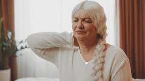 elderly senior woman sitting on bed hand massages neck pain in the back spine after waking up warm-up exercises. Lady pension age sad unhappy face, old age health care concept. emotions suffering - Powered by Shutterstock - Get 15% off with code: PIKWIZARD15
