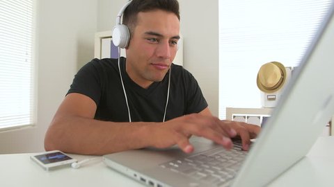 Hispanic business man listening to music in office at laptop