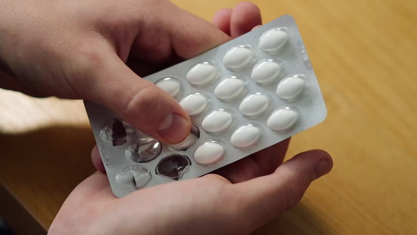 A person unpacking a white pill and preparing to take it