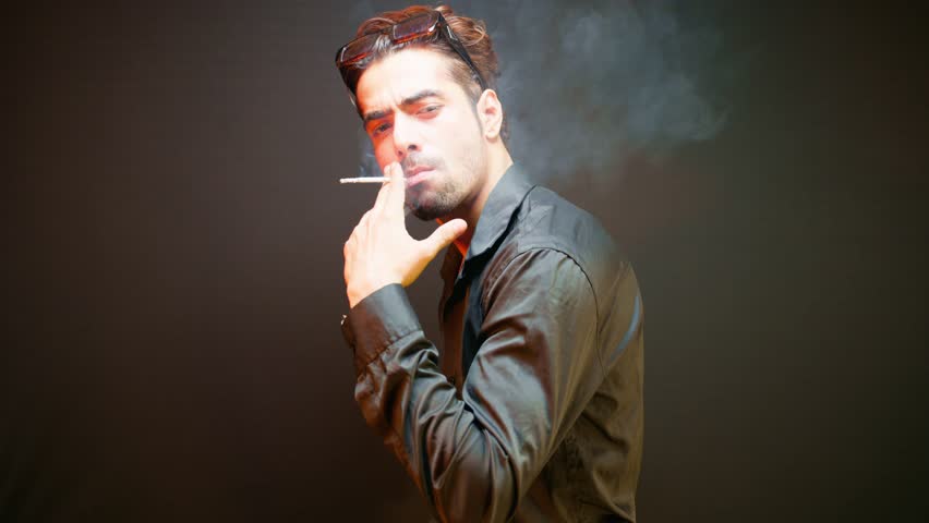 Model standing strikes a pose as enjoying his smoke, Man stands confidently while modeling with cigarette, Guy shows stance for photo collection, Captures cool style, Male looks great in the portfolio