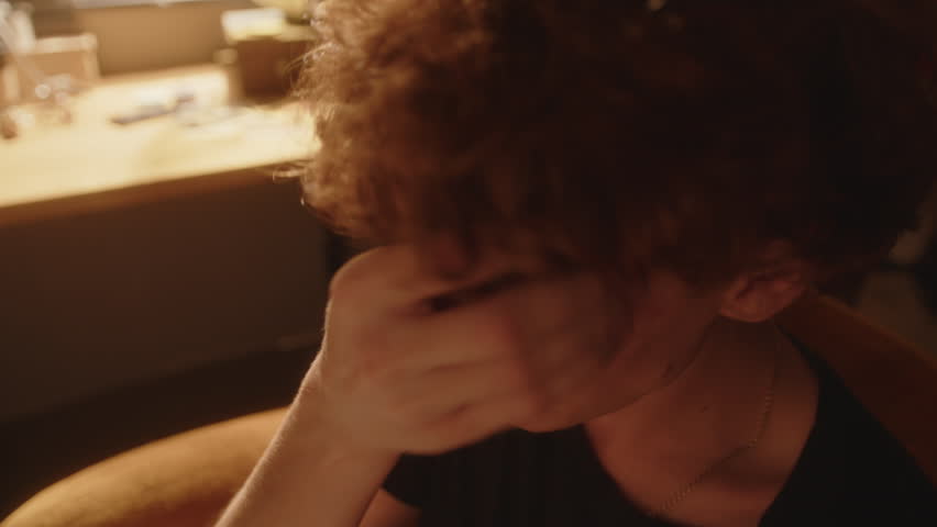 Despaired young man sitting in sunlit room, crying and wiping tears from his face in moment of sadness or depression. Close-up shot