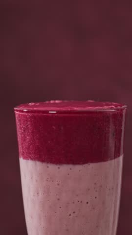 hand puts fresh berries into a colorful red and pink smoothie glass, food closeup