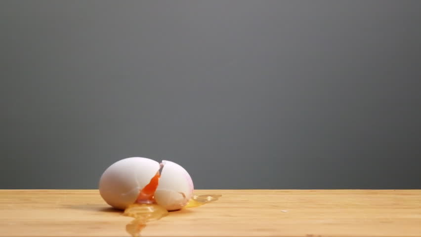 A reverse slow-motion video of a broken egg reassembling itself and jumping back onto a wooden surface. Captures a unique and mesmerizing perspective in stunning detail