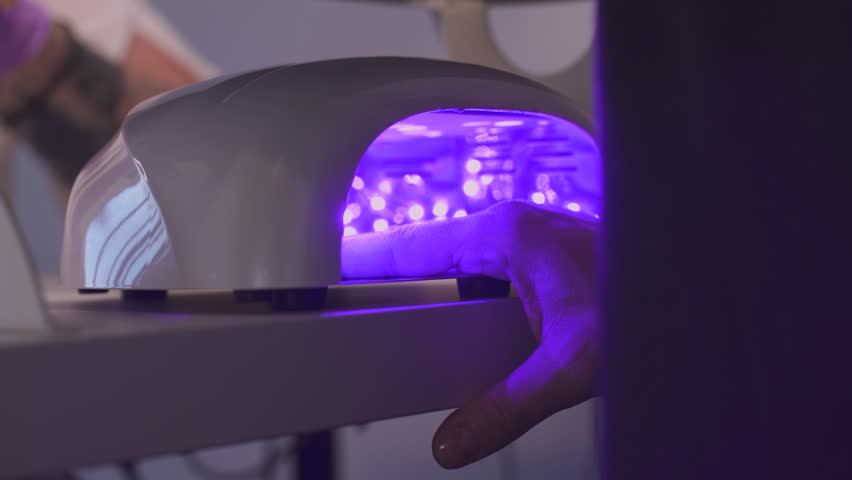 Client's hands under UV nail lamp during the gel manicure curing process