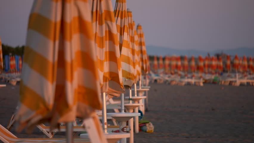 Detail umbrellas white and orange at sunset. Italian beach in summer. Panning 4K