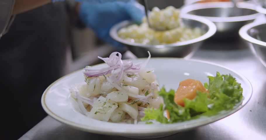 A slow-motion of adding a pile of boiled corn to a fresh Peruvian Ceviche in a white plate