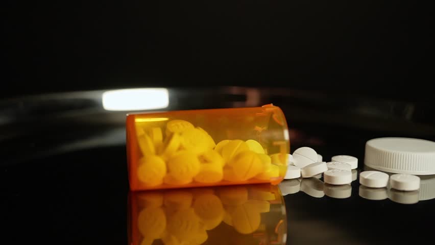 Prescription pills fall on the table from the bottle in slow motion. Pharmaceutical opioid painkillers crisis in America. Narcotic abuse adn addiction overdoses. Macro close up shot.