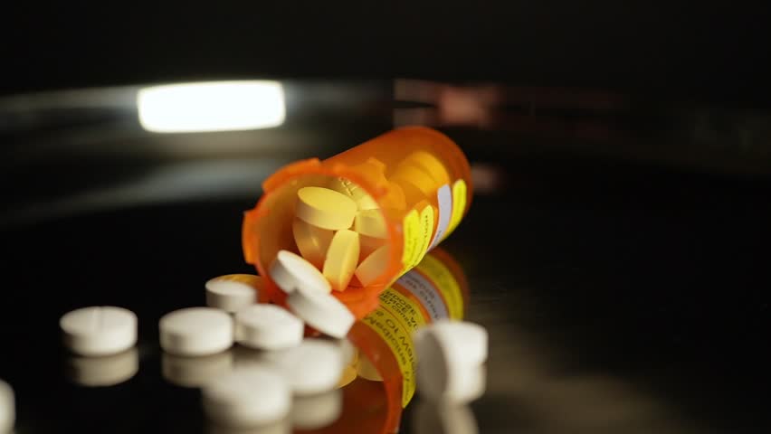 Prescription pills fall on the table from the bottle in slow motion. Pharmaceutical opioid painkillers crisis in America. Narcotic abuse adn addiction overdoses. Macro close up shot.