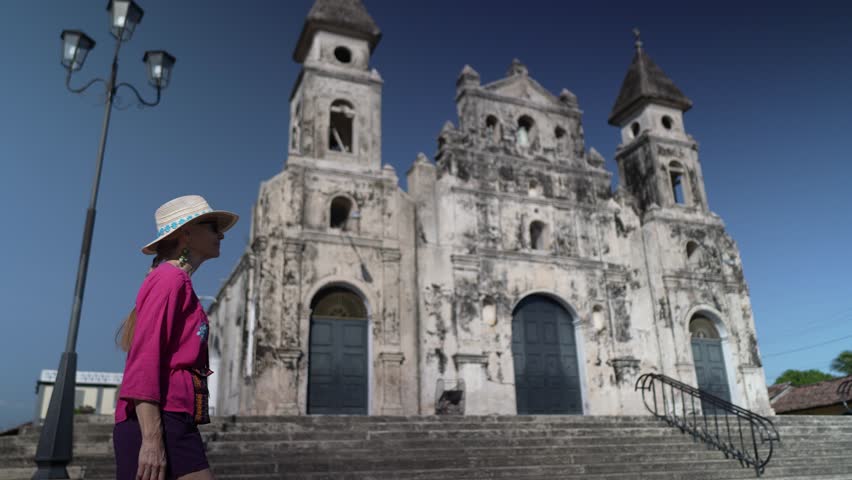 A mature woman stands in front of the historic Iglesia de Guadalupe, admiring its architecture. She enjoys a cultural experience in Granada, Nicaragua.