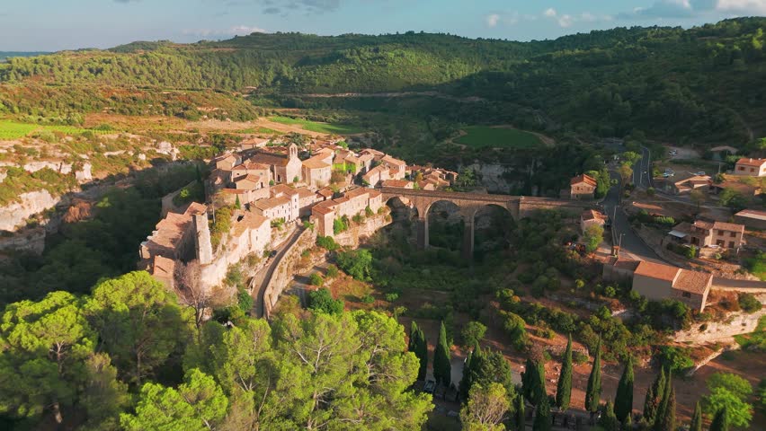 Aerial view of the medieval village of Minerve in the south of France. Historic stone buildings, a beautiful arched bridge, and a colorful rainbow in the sky.